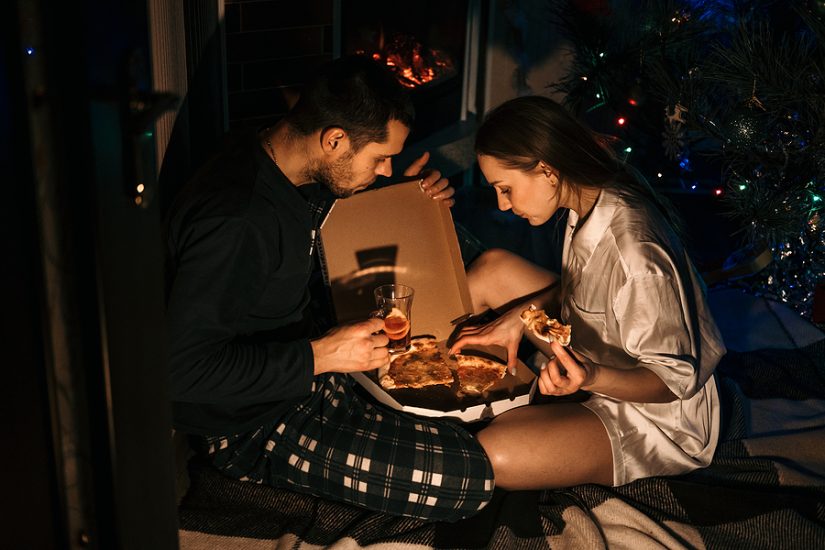 Couple enjoying a cozy Christmas date night with pizza and wine at home.