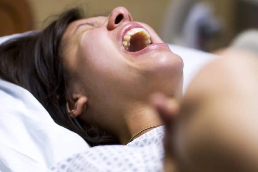 Woman in labour expressing pain and frustration in hospital bed.