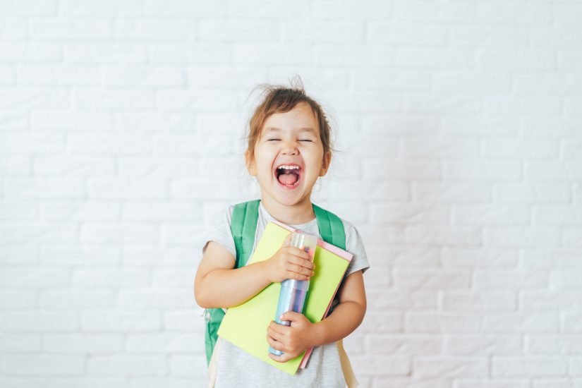 Kids with school supplies and backpack smiling.
