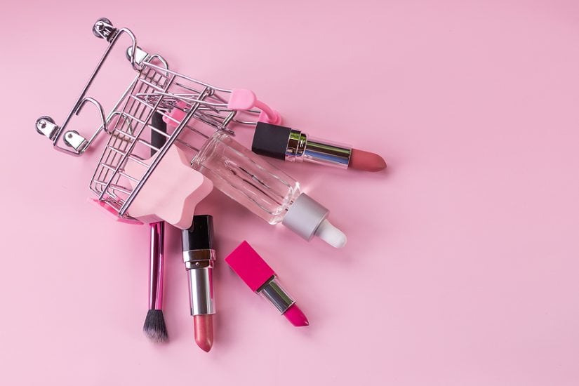 Makeup products including lipstick, brush, and skincare items in a small shopping cart.