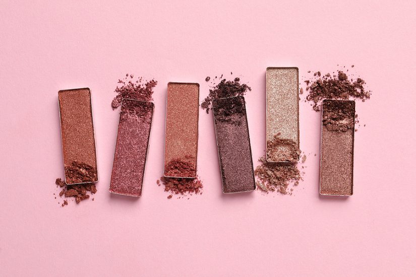 Makeup eyeshadow palette with five shades and scattered powder on pink background.