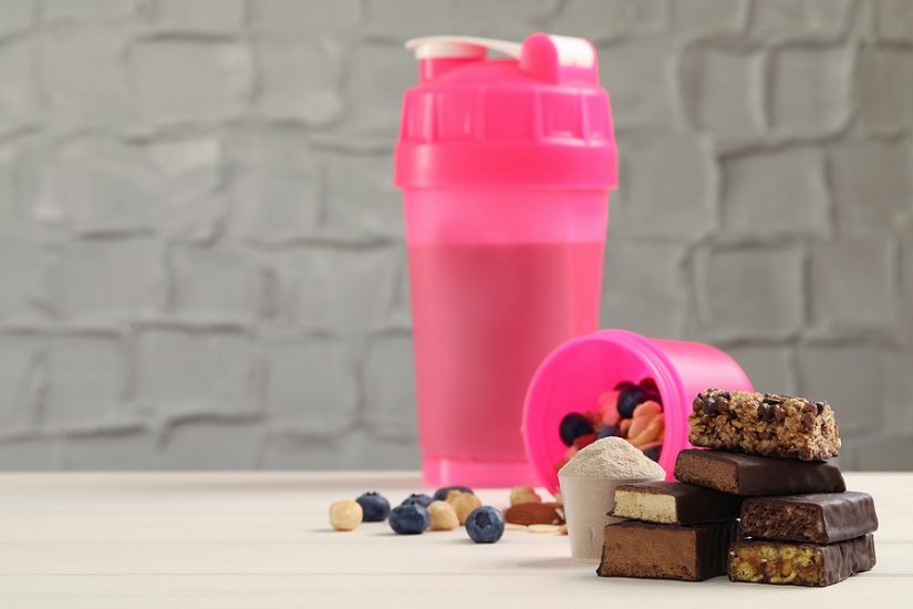 Healthy protein shake with assorted protein bars and berries in a pink shaker bottle.