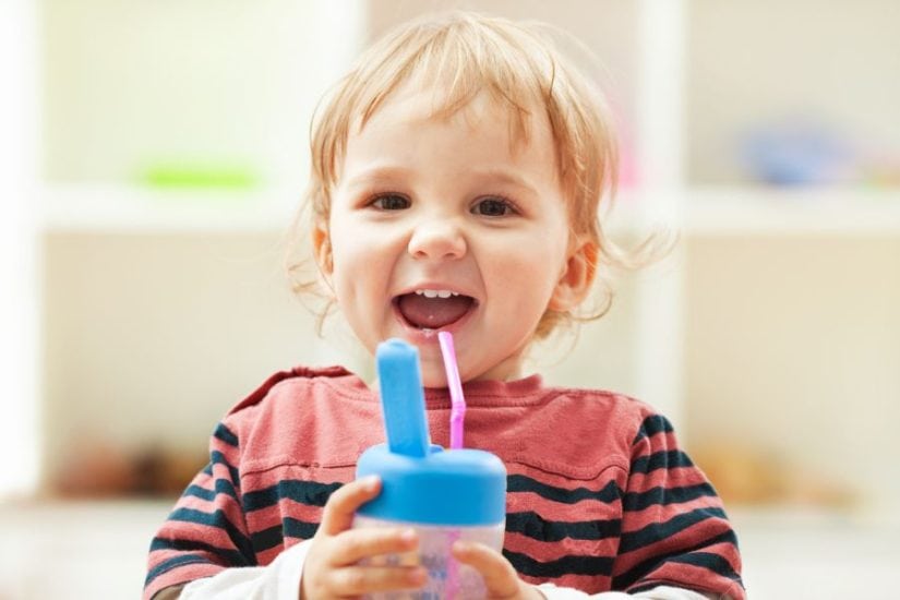 Happy toddler drinking from a sippy cup on the go.