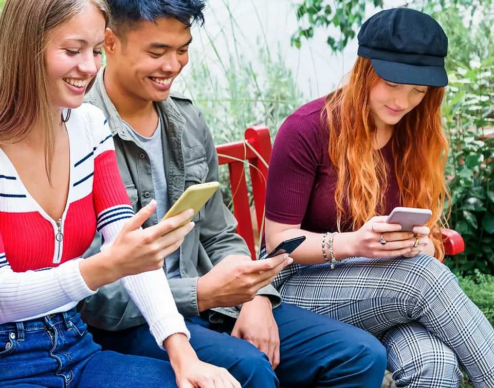 Group of young adults using smartphones outdoors, enjoying social media.