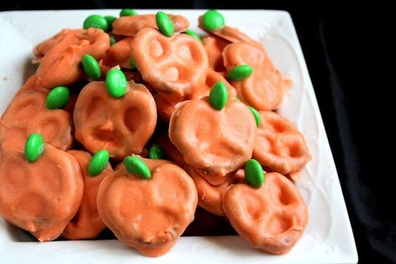 Halloween pretzel pumpkins with orange coating and green candy stems.
