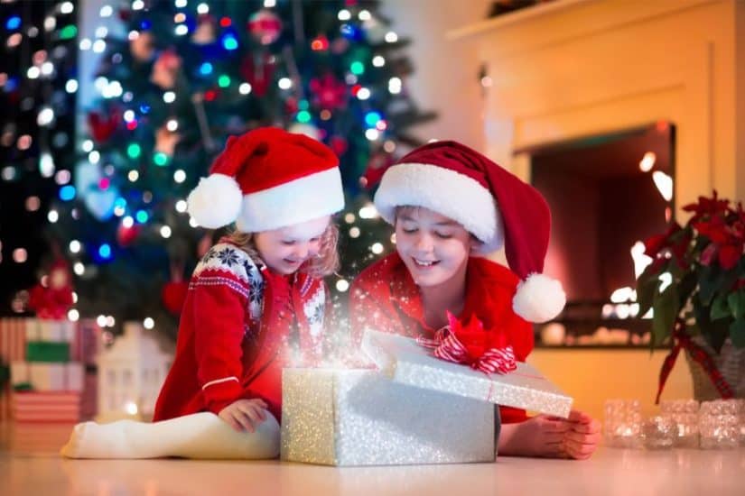Kids opening Christmas gift in front of decorated tree.