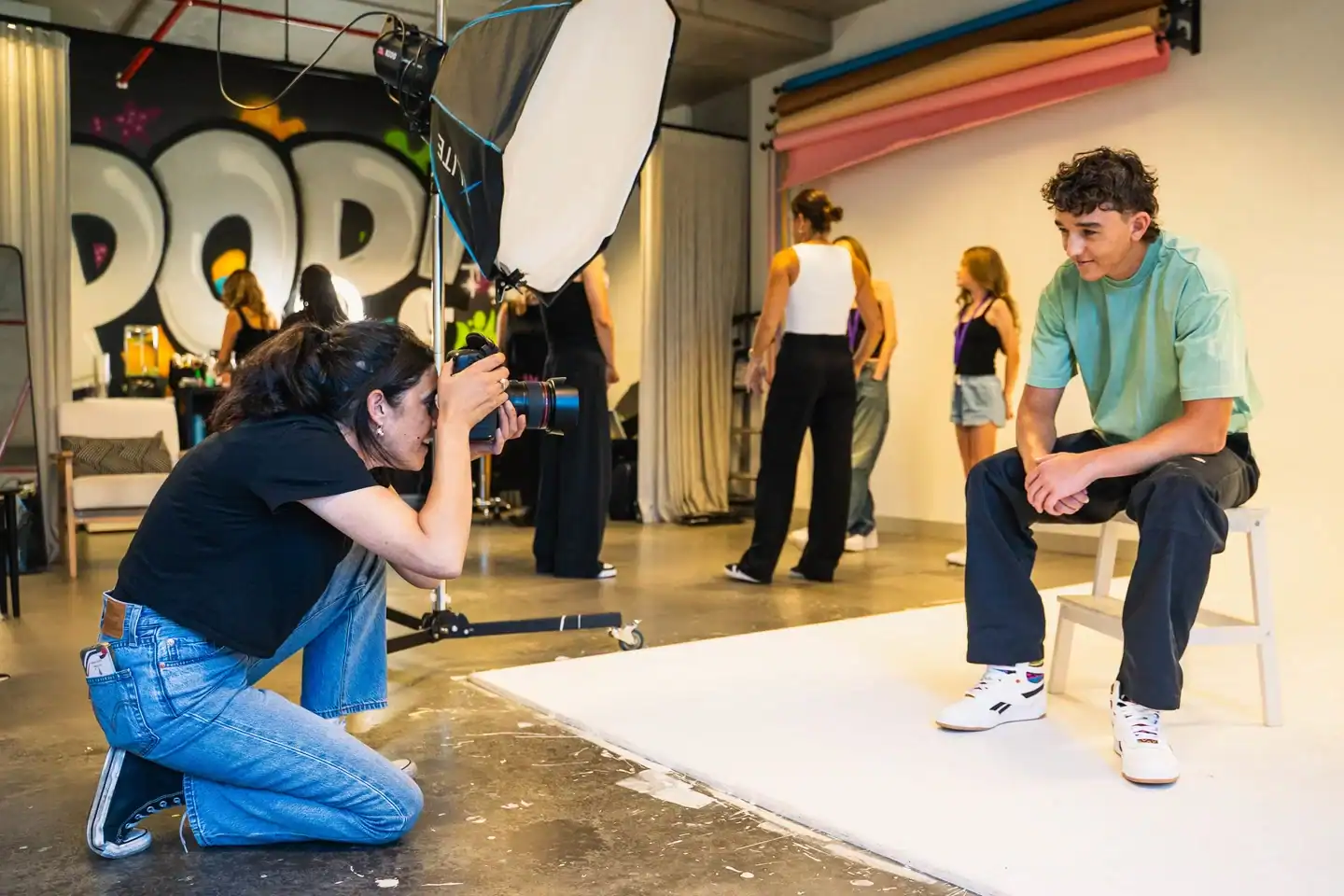 Young man sitting on a stool during a professional photoshoot in a studio setting.