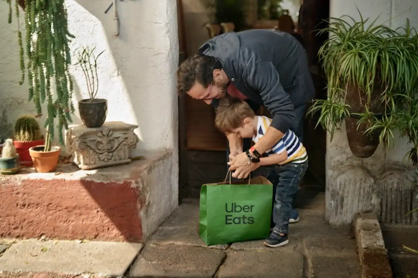Parent and child with Uber Eats bag at doorstep during school holidays.